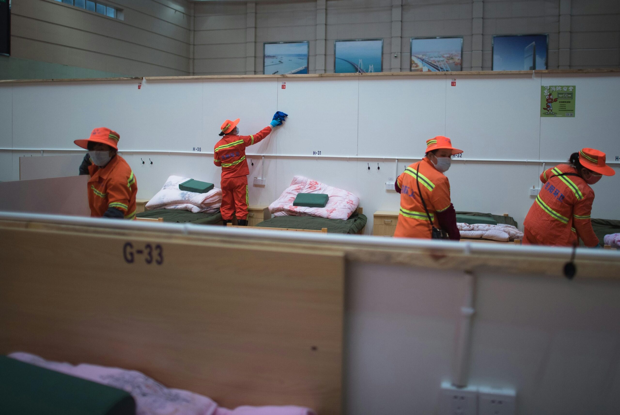 Hospital staff in orange uniforms organize and clean patient beds in a healthcare facility.